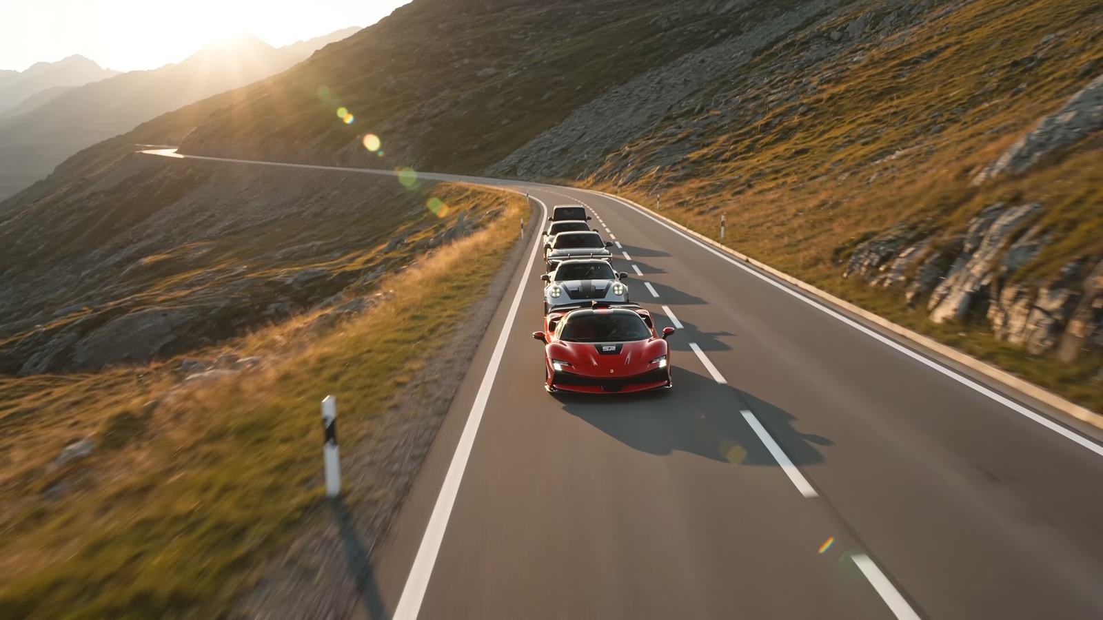 Sechs Sportwagen im Konvoi auf einer Schweizer Passstrasse im Abendlicht